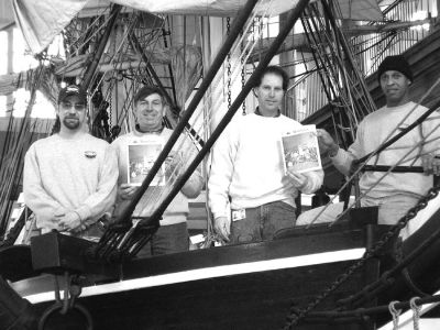 020305
Four men, including workers from the Mattapoisett Boatyard, currently working on the restoration of the half-scale model of the whale ship Lagoda at the New Bedford Whaling Museum recently posed on deck with copies of The Wanderer. Pictured here (l. to r.) are Craig Williams, Karl Collyer, Thomas Tucker, and Loulou Casi. The restoration is being conducted in stages, with the present focus being the removal of old sails and repairs to the rigging, all of which will be necessary prior to the new sails being b
