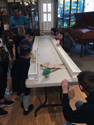 Marion Natural History Museum
One hull or two? On March 11, the Marion Natural History Museum afterschool group explored the physics behind sailboat design. Mark Whalen, engineer with Massachusetts Maritime Academy, introduced several alternative design ideas for constructing our own sailboats. The students explored a variety of hull designs, mast locations and different sizes and shapes of sails. Then they raced the vessels in rain gutters to see which design moved fastest.
