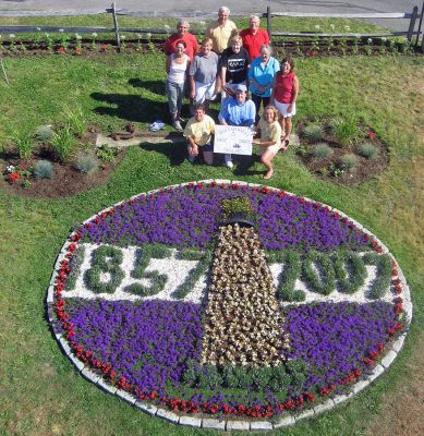 Living Logo
Members of Mattapoisetts 150th Garden Group recently posed for this aerial shot of the sesquicentennial logo they recreated out of plantings at Shipyard Park. The group members have put in countless hours planting this and other beds from Shipyard Park to Neds Point to commemorate the towns 150th birthday. This photo is also being planned as the cover for the next Annual Town Report. (Photo courtesy of Danny White).
