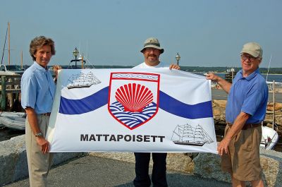 Flying the Town's Flag
(L. to R.) Mattapoisett artist Peter Martin, Mattapoisett Lions Club President Lance Calise, and Arthur Blackburn, Chairman of the Lions Club Flag Project, pose with the Mattapoisett town flag designed by Mr. Martin. The flag hangs in the Hall of Flags at the State House depicting the history and spirit of the Mattapoisett community. The Mattapoisett Lions Club will be selling flags at Harbor Days and throughout the year for $35 to benefit Lions Club charities and commemorating the Towns 150th anniversary.
